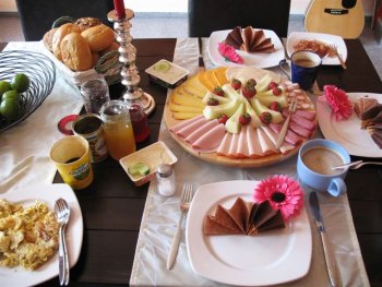 Geburtstags-Fruehstueckstisch mit Ruehrei, Speck, Obst und Milchkaffee